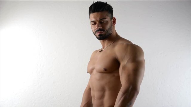 Muscular bodybuilder by empty white wall, looking at camera, with large copyspace next to him