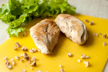 Ruddy chicken breasts with leaf salad and crushed walnut on yellow cutting board.