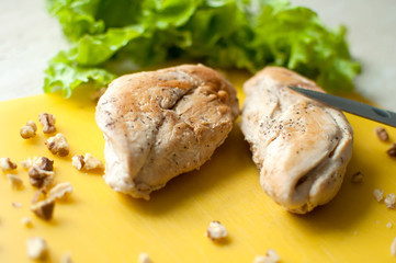 Ruddy chicken breasts with leaf salad and crushed walnut on yellow cutting board.