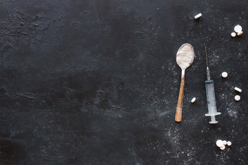 Tablets, spoon with drugs and a syringe on a black background with space for text