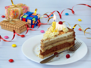 piece of chocolate banana cake decorated with rosettes of cream, berries and candles on light wooden background. Birthday.