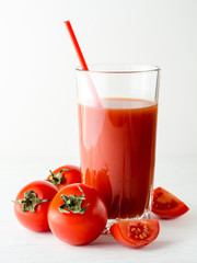 Tomato juice in glass and fresh tomatoes on white wooden table.