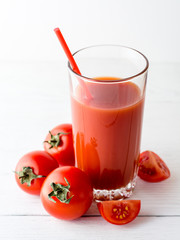 Tomato juice in glass and fresh tomatoes on white wooden table.