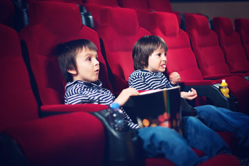 Two preschool children, twin brothers, watching movie in the cinema