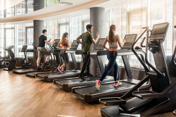 Group of four people running on treadmills in fitness gym