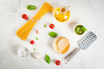 Ingredients for the preparation of Italian pasta with pesto sauce: spaghetti, olive oil, tomatoes, basil, parmesan cheese, pesto sauce, basil, garlic. On a white stone table. Copy space