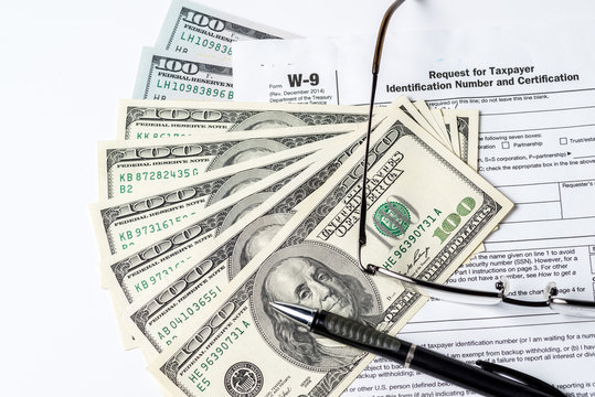 Close up image of money,$100 bills,W-9 form,glasses and a pen on white background
