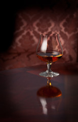Glass of brandy, cognac or whiskey standing on a reflective table in front of patterned chair