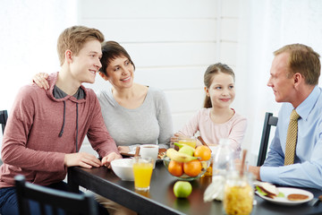Obraz na płótnie Canvas Close-knit family gathered together in kitchen, talking to each other animatedly and eating healthy breakfast, waist-up portrait