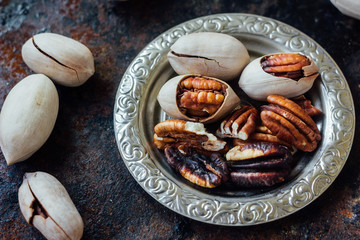 Pecan nuts on metal plate over black rustic surface.