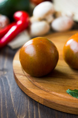 Kumato tomatoes on wooden board surrounded by vegetables.