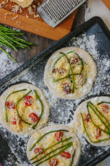 Cooking process of making mini pizza - small and personal, with cheese, tomatoes and asparagus.