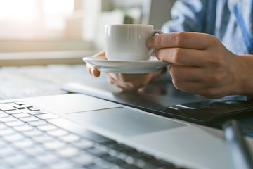 Person holding a coffee cup while working on the laptop