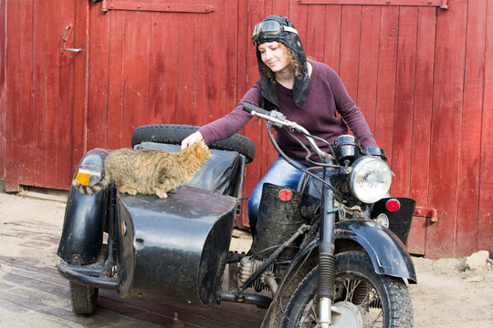 Photo of girl on a vintage motorbike in pilot cap with cat