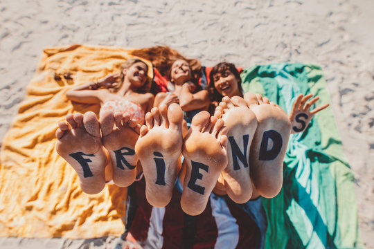 Word friends on the feet of young women lying at the beach