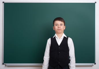 elementary school boy near blank chalkboard background, dressed in classic black suit, one pupil, education concept