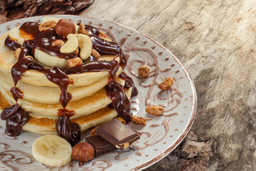 Stack of hot pancakes with nuts, bananas and chocolate syrup.