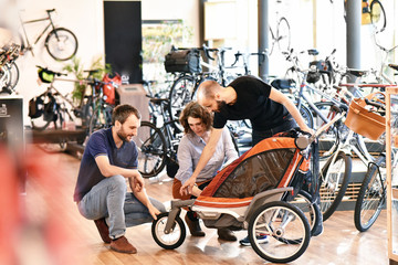 Beratung im Fahrradladen - junges Pärchen wird beim Kauf eines Kinderanhängers beraten // bicycle...
