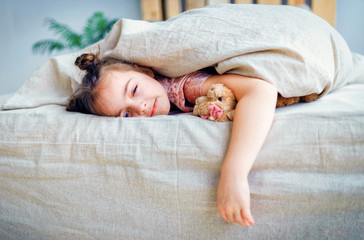child little girl sleeps in the bed with a toy teddy bear