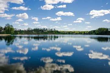 Foto op Canvas Cloudy blue sky reflects into the lake with trees on the horizon. © Igors Kuznecovs
