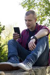 Fototapeta premium Young man sits in the park and chat via mobile phone