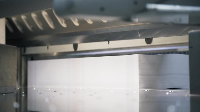 Side view of a male worker wearing a blue shirt cutting a stack of paper in a typography. Locked down real time medium shot