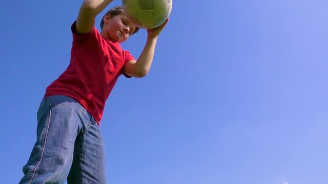 Young boy dribbles the ball against blue sky, slow motion
