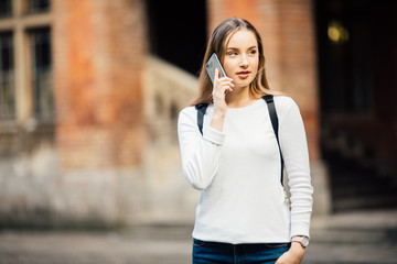 Happy student girl walking and calling on mobile phone outdoors with a Uni background