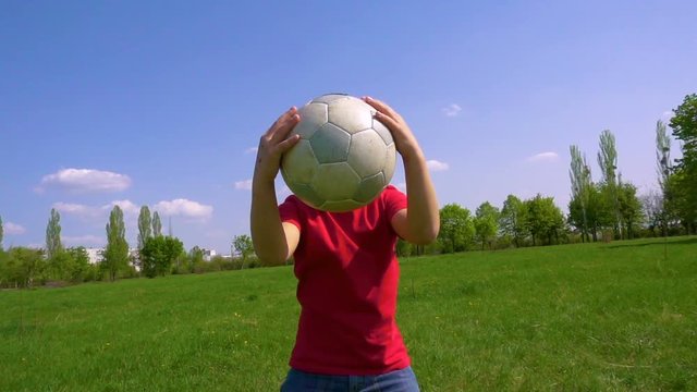 Young boy dribbles the ball on green meadow, slow motion