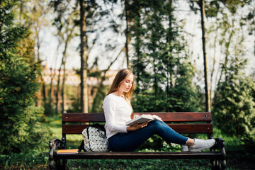 college student girl reading a book sitting on bench in city park