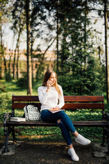 Obraz premium Young student woman uses smartphone sitting on bench in the Park.
