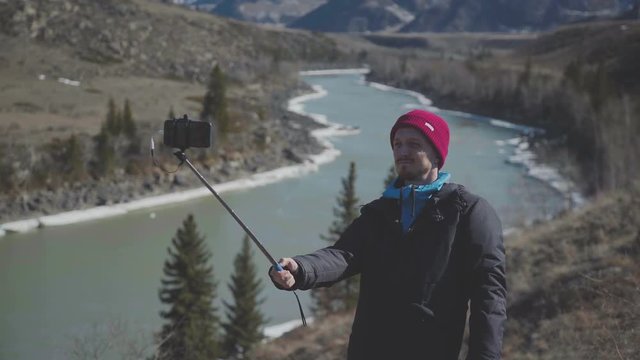 Tourist takes pictures of mountains. Selfie on the background of the mountain river. Man photographed mountains in the smartphone. Hiking. Selfie. Hiking Tourist Taking Photos Using Smartphone Device.