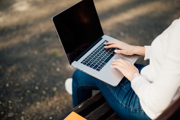 Woman sitting on bench outside and working on computer in park