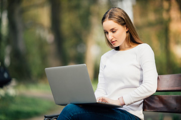 Happy student teenager girl learning with a laptop lying in a bench in an university campus