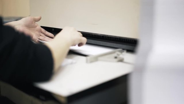 Woman worker inserting sheets of paper into a typographic machine. Locked down real time close up shot