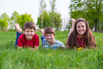 Fototapeta na wymiar Three kids lying together on green grass meadow