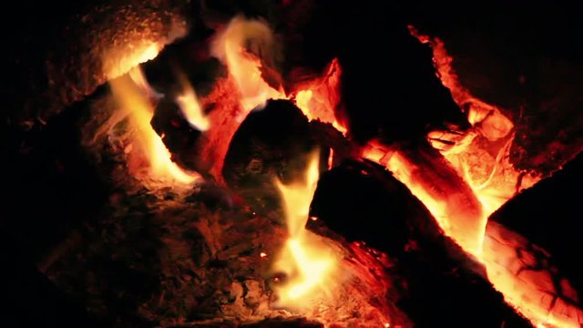 Campfire with logs and embers glowing in the dark