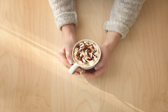 Hands of young woman with cup of tasty cocoa drink on wooden background