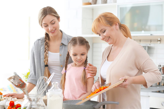 Young Woman With Mother And Daughter Cooking In Kitchen