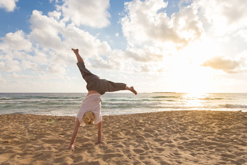 Relaxed woman enjoying sun, freedom and life turning cartwheel on beautiful beach in sunset. Young lady feeling free, relaxed and happy. Vacations, freedom, happiness, enjoyment and well being. - Powered by Adobe