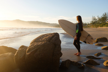 Fototapeta na wymiar Young female surfer looking at the ocean with surfboard at sunrise