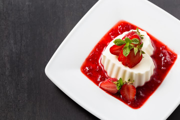 Vanilla panna cotta with strawberry jam on a white plate. Dark background. Valentine's day concept