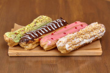 Colorful eclair cakes with cream on wooden board