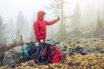 Hiker travels in the mountain forest in the mist with a backpack and trying to find a mobile...