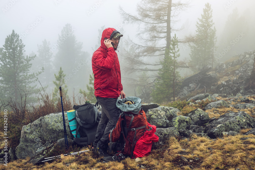 Wall mural hiker travels in the mountain forest in the mist with a backpack and trying to find a mobile connect