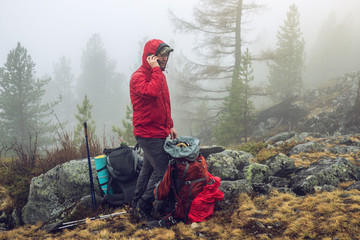 Obraz premium Hiker travels in the mountain forest in the mist with a backpack and trying to find a mobile connection