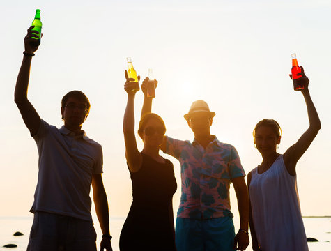 Happy friends drinking alcoholic drinks and having a party on a beach in the sunset. Man in hat enjoying a sunset on a beach and drinking a beer. Young, adult, freedom, beach, summer, concept.