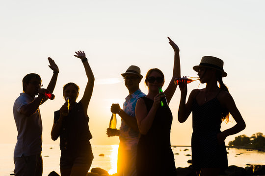 Happy friends drinking alcoholic drinks and having a party on a beach in the sunset. Man in hat enjoying a sunset on a beach and drinking a beer. Young, adult, freedom, beach, summer, concept.