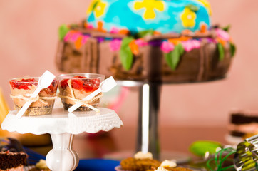 Delicious mousse covered in strawberry topping, presented inside small glasses with spoons attached, colorful cake background, pastry concept