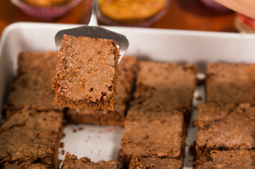 Delicious brown colored chocolate brownies lined up, square pieces as seen from above angle, metal cake cutter being used, pastry concept